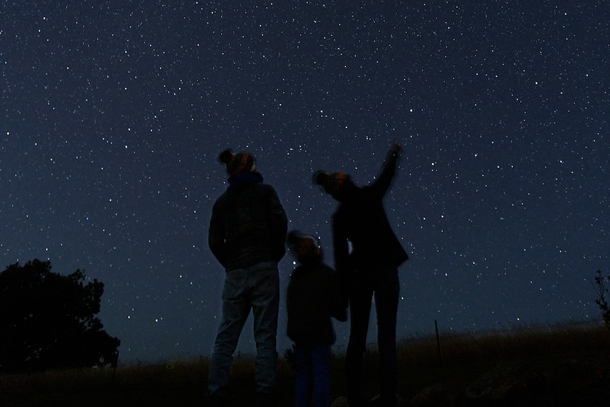 Two parents and a small child are looking at the starry sky.