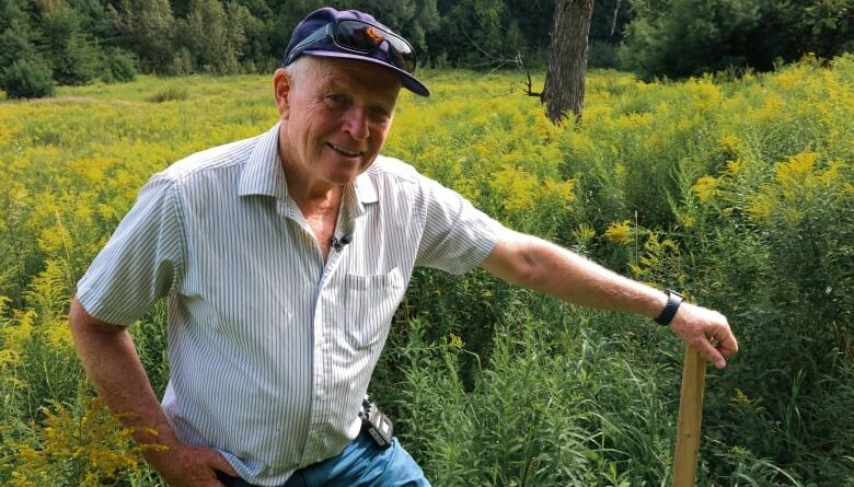 A man is standing in a field with his hand on a wooden pole