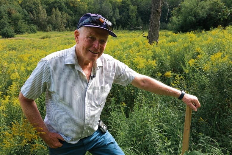 A man is standing in a field with his hand on a wooden pole